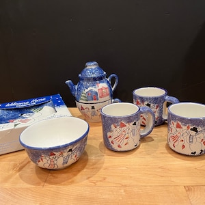 May include: A blue and white ceramic tea set with a teapot, four mugs, and a bowl. The set features a winter scene with snowmen and a house. The box says "Welcome Home" and "Snowman's Delight".