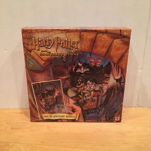 May include: A 500 piece Harry Potter and the Sorcerer's Stone mystery puzzle box. The box features a colorful illustration of Harry Potter, Ron Weasley, and Hermione Granger flying on a broomstick. The box also includes a magic decoder to reveal hidden messages.