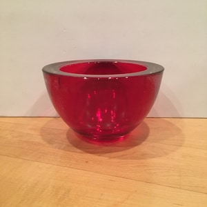May include: A red glass bowl with a rounded shape. The bowl is made of clear glass with a red tint.