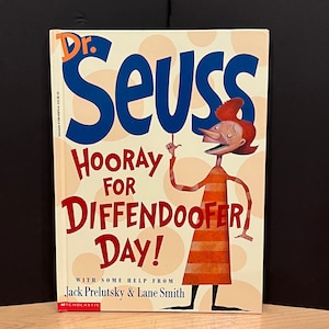 May include: A book cover with a yellow background and red, white, and blue polka dots. The title is "Dr. Seuss Hooray for Diffendoofer Day!" with some help from Jack Prelutsky & Lane Smith. The cover features a cartoon illustration of a person with red hair and a striped shirt.
