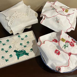May include: Set of six white cocktail napkins with green shamrock embroidery. The napkins are packaged in a white box with a green ribbon and the text "Fine Irish Linen Cocktail Mats by Arrowlow".