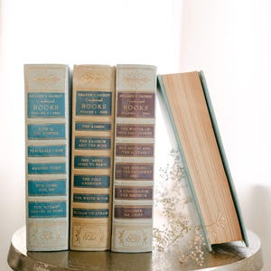 May include: A collection of vintage Reader's Digest Condensed Books. The spines are in shades of blue, beige, and gold, with titles like "Fate is the Hunter" and "The Ugly American." One book leans against the others.