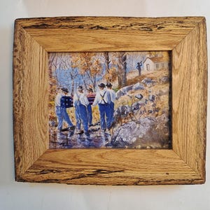 May include: A framed painting depicting four individuals in white shirts and blue trousers carrying a casket draped in an American flag through a rocky, wooded landscape. The scene includes a small building in the distance and a wooden frame.