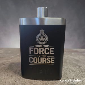 May include: Black Yeti flask with a silver top. The flask features the Durham Regional Police logo and the text "FROM THE FORCE TO THE COURSE." The flask is a sleek, rectangular shape.