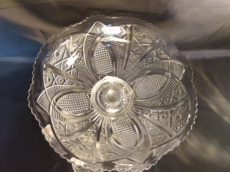 Puede incluir: Un cuenco de cristal transparente con pedestal, borde festoneado y dise&ntilde;o de cristal tallado intrincado. El cuenco tiene un pedestal central con una base circular.