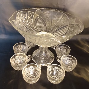 Puede incluir: Un juego de ponchera de cristal vintage con un cuenco de cristal transparente y ocho tazas a juego. El cuenco tiene un dise&ntilde;o decorativo de cristal tallado y una base de pedestal. Las tazas tambi&eacute;n son de cristal tallado y tienen un asa.