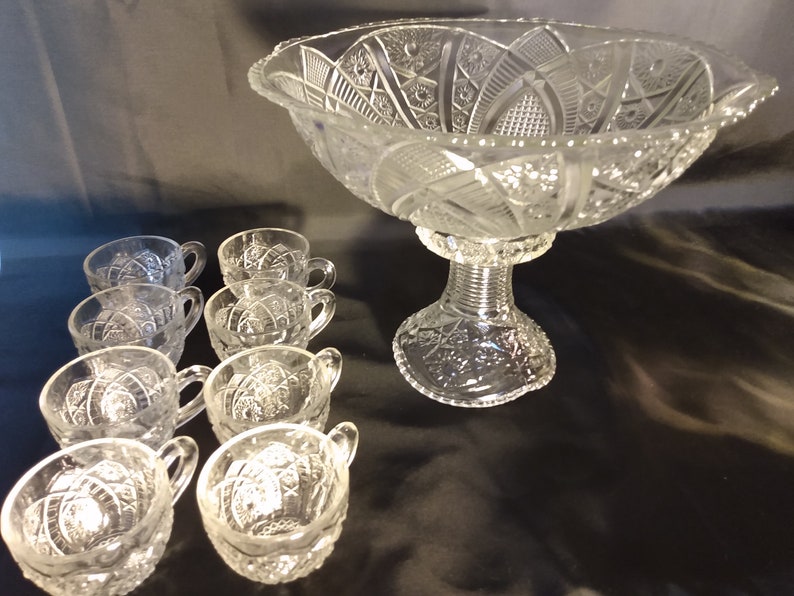 Puede incluir: Un juego de ponchera de cristal vintage con un cuenco grande y transparente con base de pedestal y ocho tazas a juego. El cuenco y las tazas tienen un dise&ntilde;o de cristal tallado.