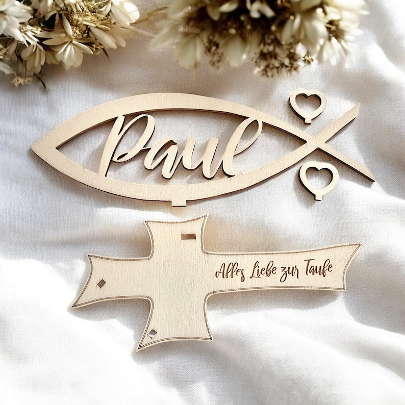 May include: Wooden cutout of a fish with the name "Paul" inside and two hearts. Below is a wooden cross with the text "Alles Liebe zur Taufe".