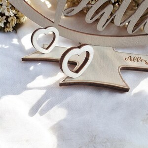 May include: Two wooden heart-shaped ornaments with a cutout design. The ornaments are on a wooden base with the word "Alles" engraved on it.