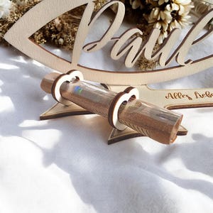 May include: A wooden money holder with the word "Paul" carved into it. The holder is shaped like a fish and has a slot for a rolled bill. The text "Alles Liebe" is also carved into the wood.