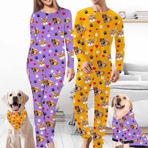 May include: Matching purple and yellow pajama sets with cat, dog, paw print, and heart patterns. A dog wears a matching bandana, and another dog wears a matching pajama top. The pajamas are long-sleeved and long-legged.