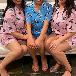 Peut inclure: Trois personnes portant des pyjamas assortis avec un imprim&eacute; de chien. Les pyjamas sont roses et bleus avec un col blanc. Les personnes sont assises sur un canap&eacute; blanc.