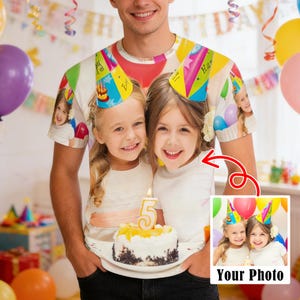 Puede incluir: Una camiseta blanca con una foto personalizada de dos niñas pequeñas con gorros de fiesta, sosteniendo un pastel de cumpleaños con una vela encendida. La camiseta tiene un tema de cumpleaños colorido con globos y serpentinas.