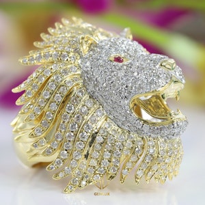 May include: A gold lion ring with a white diamond-encrusted head and a ruby eye. The lion's mane is detailed with gold and diamonds. The ring is a statement piece of jewelry.