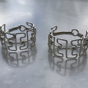 Könnte beinhalten: Zwei silberne Ringe mit geometrischem Design. Die Ringe sind aus Draht gefertigt und haben die Form des Buchstabens "F".