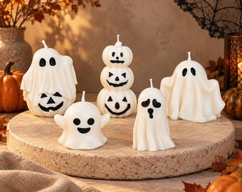 Könnte beinhalten: Ein Set aus fünf weißen Wachskerzen in Halloween-Formen, darunter Geister und ein Stapel aus drei Kürbissen. Jede Kerze hat einen Docht und schwarz bemalte Gesichtsmerkmale wie Augen und Münder und ist auf einem runden Steinsockel platziert.