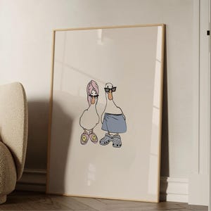 May include: A framed art print featuring two cartoon ducks. One duck wears a pink towel and sunglasses, the other wears sunglasses, a blue towel, and Crocs. The ducks are drawn in a minimalist style.