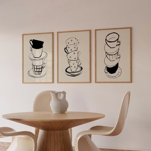 May include: Three framed black and white illustrations of stacked teacups on a white wall. The teacups are drawn in a simple, minimalist style. The frames are light wood.