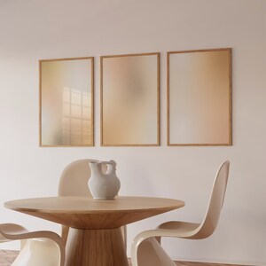 May include: A contemporary dining area with a round wooden table and cream-coloured chairs. A white ceramic vase is on the table. Three framed abstract artworks with gradient colour schemes hang on the wall. The table is approximately 120 cm in diameter.