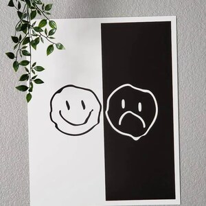 May include: A black and white print with a smiley face on the left side and a frowning face on the right side. The print is divided in half with a black background on the right and a white background on the left.