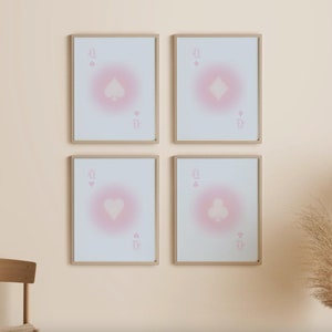 May include: Four framed prints of playing cards with a pink gradient background. Each print features a different suit: spades, diamonds, hearts, and clubs. The cards are all queens.