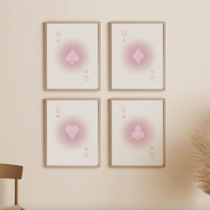 May include: Four framed prints of playing cards with a pink gradient effect. Each print features a different suit: spades, diamonds, hearts, and clubs. The prints are arranged in a grid pattern on a light beige wall.