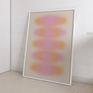 Puede incluir: Impresión de arte abstracto con un marco blanco. La impresión presenta un diseño borroso de formas superpuestas de color rosa y naranja.