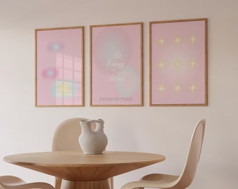 Peut inclure: Trois impressions encadrées avec des fonds roses et du texte blanc. L'impression de gauche a un design flou aux couleurs pastel. L'impression du centre a le texte "Be the Energy You Want to Attract". L'impression de droite a un motif d'étoiles blanches.