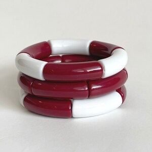 May include: Three stacked bracelets made of red and white plastic beads. The bracelets are made of alternating red and white beads.