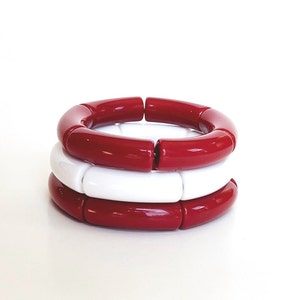 May include: Three stacked bracelets made of red and white ceramic beads. The bracelets are round and have a glossy finish.