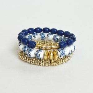 May include: A set of three bracelets featuring blue and white ceramic beads with a floral pattern, and a gold metal spacer bead.