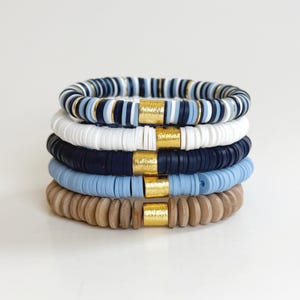 May include: Stack of six bracelets with blue, white, and brown beads. The beads are interspersed with gold spacers.