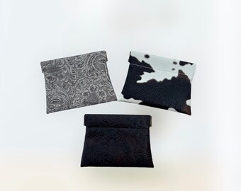 May include: Three small pouches with different patterns. One pouch is black with a floral embossed design, one is gray with a floral embossed design, and one is black and white with a cow print design.