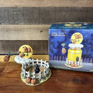 Peut inclure: Un ensemble de décorations de bougies sur le thème d'Halloween avec un chat noir, des citrouilles et une clôture blanche. L'ensemble comprend un dessus de pot, une petite base ronde et une boîte avec le texte "Kathy Hatch Escape From Pumpkin Patch".