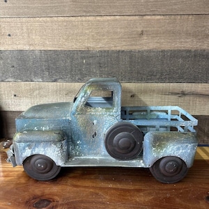 May include: A blue and green metal toy truck with a distressed finish. The truck has a flatbed with a metal grate and a rusty look.