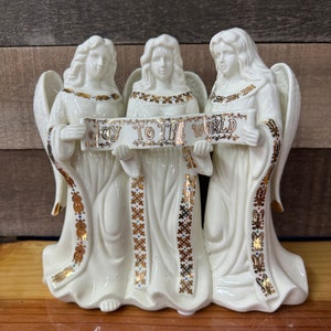 May include: Three white porcelain angels with gold accents holding a banner that reads "Joy to the World".
