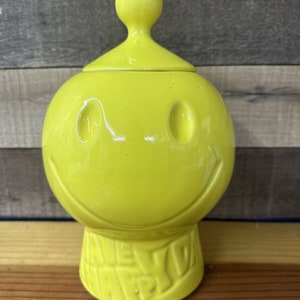 Könnte beinhalten: Eine gelbe Keramikdose mit einem Smiley-Gesicht und den Worten "New York" auf dem Boden.