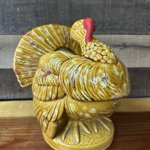 May include: A ceramic turkey figurine with a brown and yellow glaze. The turkey has a red wattle and a detailed feathered tail.