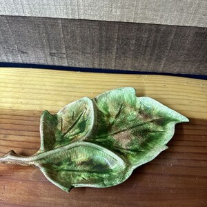 May include: A green ceramic leaf-shaped dish with brown and green glaze. The dish has three sections.