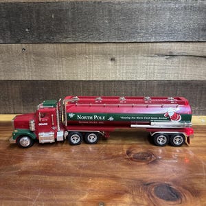 May include: A red and green toy truck with a tanker trailer. The tanker is labelled "North Pole Home Fuel Oil" with the text "Keeping You Warm Until Santa Arrives." The truck has the Sears logo.