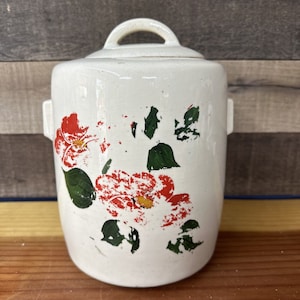 Puede incluir: Tarro de galletas de cerámica blanca con un diseño floral. El tarro tiene una tapa y está decorado con flores rojas y verdes.
