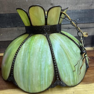 May include: A vintage green and yellow stained glass lamp shade with a decorative metal frame and chain. The shade has a floral design and is likely for a ceiling light fixture. The glass has a marbled effect.