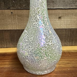 May include: A pear-shaped vase covered in a mosaic of small, iridescent glass tiles. The tiles feature a cracked, reflective finish that shifts between white, silver, and subtle pastel hues, creating a shimmering effect across the entire surface.