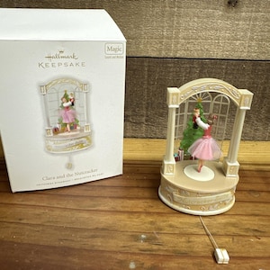 May include: A Hallmark Keepsake Clara and the Nutcracker ornament featuring a figure in a pink tutu holding a nutcracker before a Christmas tree, housed in an arched frame. The white box displays the product name and Magic sound and motion text.