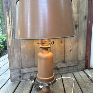 Può includere: Una lampada da tavolo marrone con un paralume in tessuto marrone e una base in legno. La lampada ha un design decorativo attorno alla base.