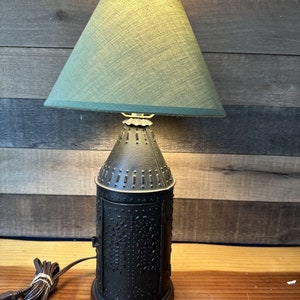 May include: A black metal table lamp with a green fabric lampshade. The lamp base is decorated with a textured pattern and has a brown wooden base.