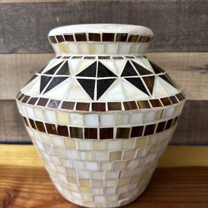 Könnte beinhalten: Eine kleine, weiße Keramikvase mit einem geometrischen Mosaikmuster. Das Mosaik besteht aus kleinen, quadratischen Fliesen in Braun-, Schwarz- und Weißtönen.