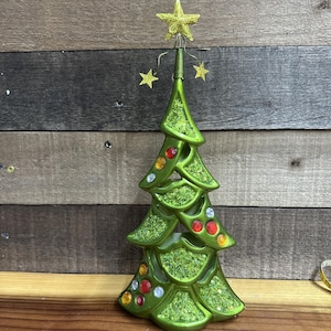 May include: A green Christmas tree decoration with a glittery texture and colorful jewel accents. The tree is topped with a gold star and has smaller gold stars attached. The tree is approximately 10 inches tall.