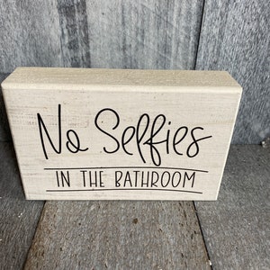 May include: A white wooden sign with black text that reads "No Selfies in the Bathroom".