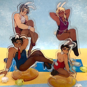 May include: Four acrylic standees featuring illustrated characters wearing bunny ears and leotards. One character wears a blue leotard with a red tie, another a red leotard, one a purple leotard with chains, and one a maroon leotard with a white ruffled collar.